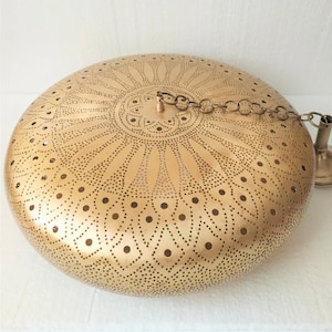 Puede incluir: Una l&aacute;mpara de techo de metal dorado con una pantalla redonda y abovedada. La pantalla tiene un patr&oacute;n decorativo intrincado de peque&ntilde;os agujeros y un dise&ntilde;o floral.