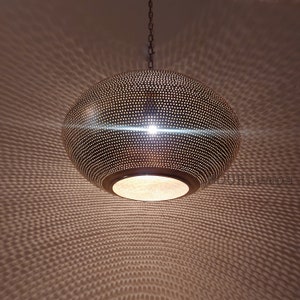 May include: A round, brass pendant light fixture with a perforated design. The light is hanging from a chain and casts a patterned shadow on the ceiling.