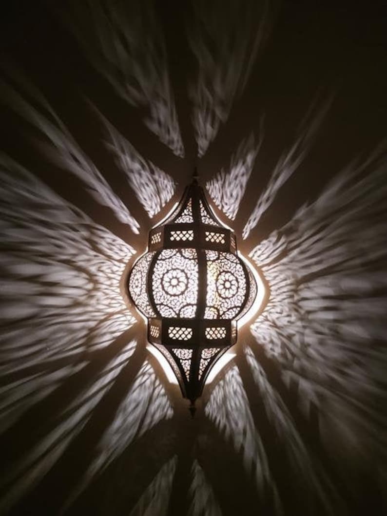 May include: A decorative metal lantern with intricate cutouts casts intricate shadows on the ceiling. The lantern is made of brass and has a traditional Moroccan design.