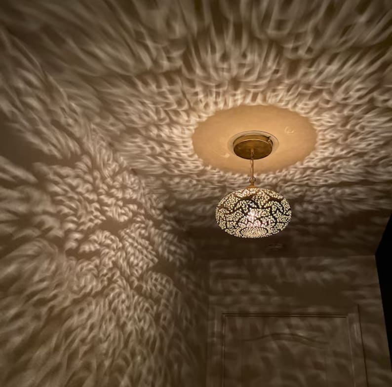 May include: A decorative pendant light fixture with a patterned metal shade, casting intricate light and shadow patterns on the ceiling and walls. The fixture is suspended from a circular ceiling mount.