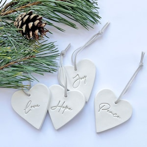 以下が含まれることがあります： 「Love」、「Hope」、「Joy」、「Peace」の文字が刻まれた白いセラミック製のハート型のオーナメント4つ。各オーナメントには、吊り下げ用の白い紐が付いています。