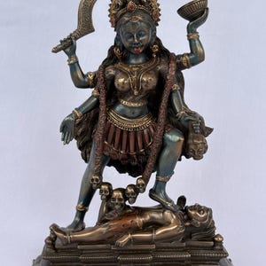 Peut inclure: Une statue en bronze de la divinité Kali à quatre bras, tenant une lame incurvée et un bol. La figure porte une guirlande de crânes, a une langue rouge saillante et se tient debout sur une figure allongée sur une base rectangulaire ornée.