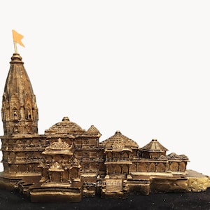 May include: A detailed, gold-coloured miniature temple with multiple structures and a tall spire topped with a small orange flag. The model sits on a black base, showcasing intricate architectural details.