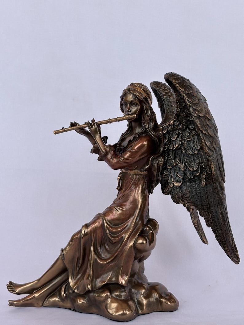 May include: A bronze-toned statue of a winged figure sitting on a cloud-like base. The figure has long hair, wears a flowing robe, and holds a flute to their lips. Large, detailed feathered wings extend from the back of the figure.