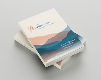 Puede incluir: Dos ejemplares apilados del libro "The Menopause Positivity Planner". La portada presenta una ilustración de estilo acuarela de montañas en tonos azules y melocotón. El título está escrito en una fuente cursiva y el subtítulo es "Putting the "Me" back into menopause" por Sarah Banks.