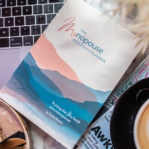 Op de afbeelding: Een wit boek met een blauw en roze aquarelontwerp op de omslag. Het boek is getiteld "The Menopause Positivity Planner: Putting the "Me" Back into Menopause" door Sarah Banks.