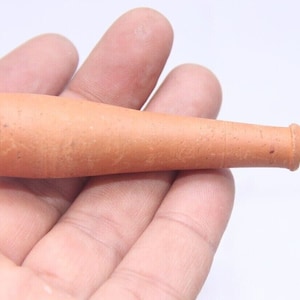 Puede incluir: Una pipa de arcilla de terracota, de aproximadamente 10 cm de largo, con una abertura ligeramente acampanada en un extremo y una abertura más estrecha en el otro extremo.