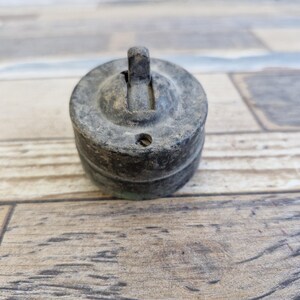 May include: An antique, round, metal light switch with a lever. The switch is a dark, weathered gray color, showing signs of age and use. The lever is raised, indicating the switch is in the on position. The switch is likely from an older home or building.