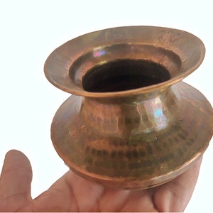 Puede incluir: Una pequeña olla de latón antigua con un borde ancho y acampanado y un cuerpo redondeado. La olla tiene un acabado martillado y una pátina de la edad.