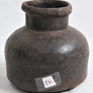 Puede incluir: Una olla de cerámica marrón oscuro con cuerpo redondeado y una abertura ligeramente acampanada. La olla tiene una superficie rugosa y texturizada y está etiquetada con el número "P2".