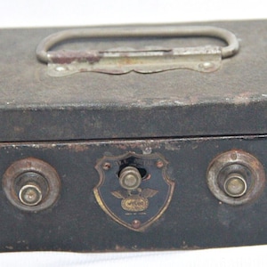May include: A black metal coin bank with a silver handle and two keyholes. The bank has a shield-shaped emblem with the words "Royal Safe" and "Made in USA".