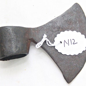 Op de afbeelding: Een roestige, grijze metalen bijl met een afgeronde handgreep. De bijl heeft een label met het nummer "N12" eraan.