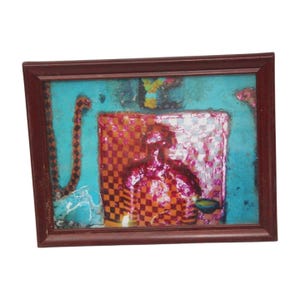 May include: Abstract artwork in a dark brown wooden frame. The art features a figure with a checkered orange and red pattern, set against a turquoise background. A checkered pattern in white and pink is also visible.