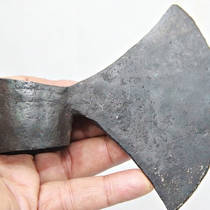 Puede incluir: Un hacha vintage con una cabeza de metal gris oscuro y un mango de madera. La cabeza del hacha es ligeramente curvada y tiene un borde afilado.