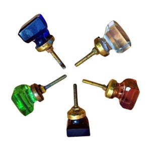 May include: Five vintage glass cabinet knobs with brass bases and screws. The knobs are in various colours, including blue, green, clear, and amber.