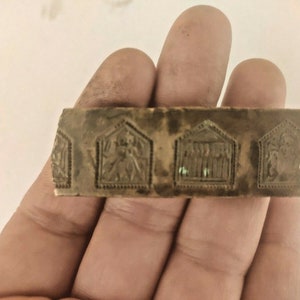 May include: A close-up of a rectangular, brown metal stamp with four raised, rectangular designs. Each design features a different image, including a person, a group of people, and a bird.