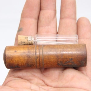 May include: A wooden needle case with a small glass vial with a cork stopper. The case is brown and has a grooved design. The vial is clear and empty.