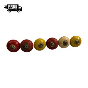 May include: A row of six colorful cabinet knobs. The knobs are round with a brass-colored center and come in red, yellow, and cream colors. The image also includes the text "FREE SHIPPING" with a graphic of a truck.