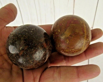 Puede incluir: Dos esferas de piedra pulidas, una con un patrón de mármol marrón y negro y la otra con un patrón de mármol rojo, marrón y dorado.