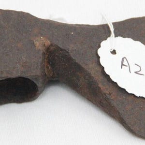 Puede incluir: Una cabeza de hacha de hierro forjado a mano, oxidada, con un agujero para el mango. La cabeza del hacha está etiquetada con "A21".