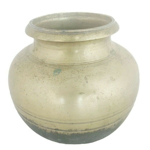 May include: A round, brass pot with a wide mouth and a slightly flared rim. The pot has a worn, aged patina and is slightly tarnished.