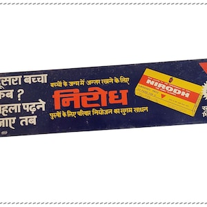 May include: A blue and white sign with the text "दूसरा बच्चा कब? पहला पढ़ने जाए तब" and "निरोध" in Hindi. The sign also features a yellow and red box with the text "NIRODH" and "SUBSIDISED PRICE FOR FAMILY PLANNING" in English. The sign is advertising a family planning product.