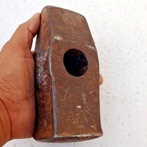 Può includere: Un martello robusto e arrugginito con un grande foro nella testa. Il martello è in metallo e ha un aspetto usurato e invecchiato.