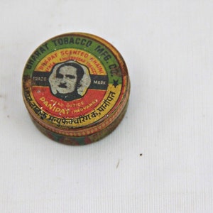 Puede incluir: Un contenedor redondo de hojalata amarillo, rojo y verde con una imagen de un hombre y el texto "Bharat Tobacco MFG. Co. Trade Mark" y "Panipat (Haryana)".