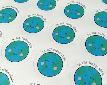 May include: A sheet of white paper with multiple round stickers featuring a cartoon earth with a smiling face and the text "I'm 100% biodegradable".