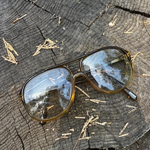 May include: Aviator sunglasses with a translucent amber-brown plastic frame and a double bridge design. The lenses are tinted in a gradient brown shade, and the temple arm features the word ZEISS printed in white lettering on the inner side.