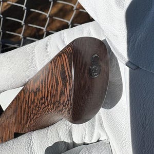 Op de afbeelding: Close-up van een golfclubkop met een donkerbruin houtnerfpatroon. De clubkop heeft een afgeronde vorm en een donker metalen embleem. De club wordt vastgehouden in een witte leren handschoen.