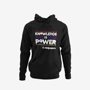 Puede incluir: Sudadera con capucha negra con un gráfico colorido que dice "Knowledge is Power" con un pequeño logotipo que dice "Nerdy Gangsta".