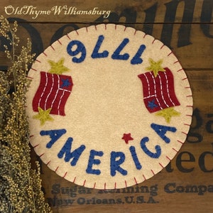 May include: A round felt wall hanging with red, white, and blue stars and stripes. The text "9111 AMERICA" is stitched in blue on a cream background.