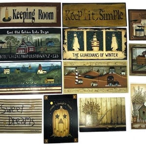 May include: A collection of folk art signs and paintings. The signs include text like "Keeping Room" and "Keep it Simple." The paintings depict scenes with houses, lighthouses, and snowmen. One painting features a pumpkin with stars.