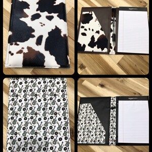 May include: A black and brown cow print folder with a black and white guitar and record pattern on the inside. The folder has a pocket on the inside and a pen holder. The folder is open and the inside is visible. The folder is made of leather and has a professional look.