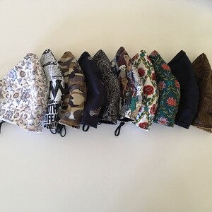 May include: A collection of 10 fabric face masks with various patterns, including floral, geometric, and abstract designs. The masks are all in different colours, including black, white, brown, green, and blue.