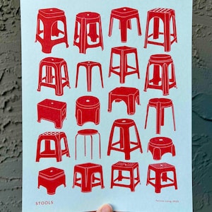 May include: A print featuring a collection of red stools in various designs against a light blue background. The word "STOOLS" is printed at the bottom left. The artist's name and year are printed at the bottom right.