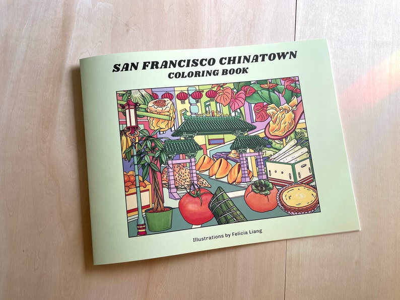 Peut inclure: Un livre de coloriage vert avec le titre "San Francisco Chinatown Coloring Book" et des illustrations d'une sc&egrave;ne de rue de Chinatown avec des lanternes, de la nourriture et des plantes. Le livre est de Felicia Liang.