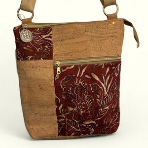 May include: A brown cork and red floral patterned crossbody bag with a gold zipper and a gold metal accent.