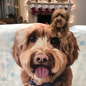 May include: A brown and white dog with its tongue sticking out is printed on a white fleece blanket with a blue snowflake pattern. The dog is looking directly at the camera.
