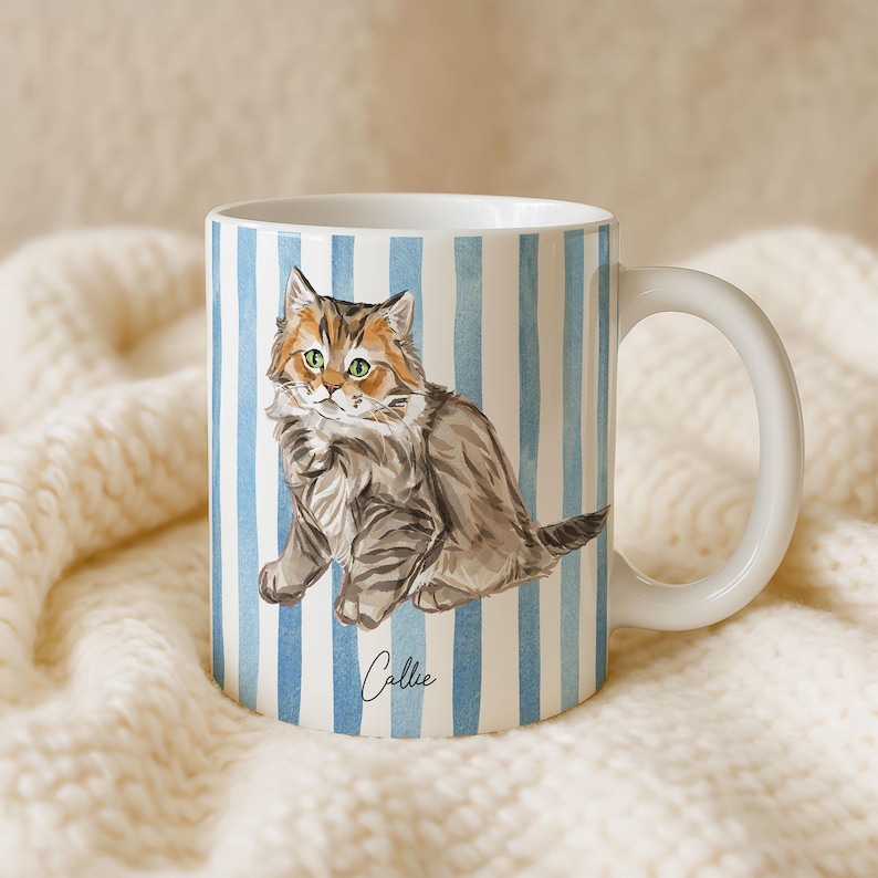 Puede incluir: Taza de cer&aacute;mica blanca con una ilustraci&oacute;n a la acuarela de un gato con ojos verdes y pelaje marr&oacute;n y gris. La taza tiene rayas verticales azules y blancas y el nombre "Callie" en cursiva.