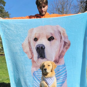 May include: A blue fleece blanket with a large golden retriever dog printed on it. The dog is wearing a blue and white striped bandana. A smaller golden retriever puppy is sitting in front of the larger dog.