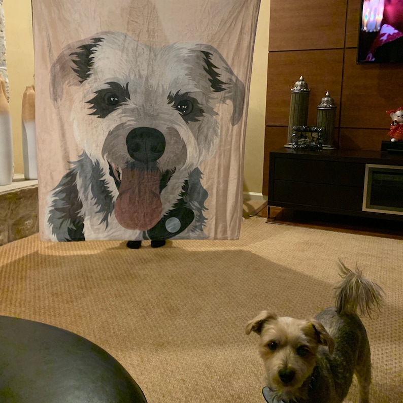 May include: A brown and white dog blanket with a close-up image of a dog's face. The dog has a black nose and tongue sticking out. A small brown and white dog is standing in front of the blanket.