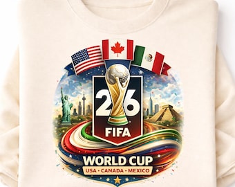 May include: Cream-colored sweatshirt featuring a colorful graphic for the 2026 FIFA World Cup, hosted by USA, Canada, and Mexico. The design includes the World Cup trophy, flags, and cityscapes of iconic landmarks.