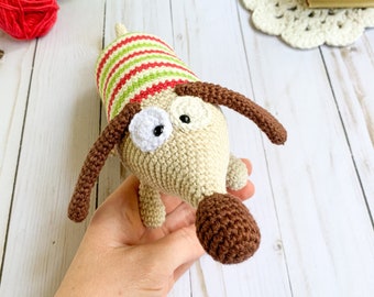 May include: A crocheted dog toy with brown ears, a brown nose, and white eyes. The dog is wearing a red and green striped shirt.