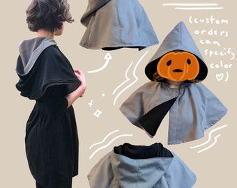 May include: A hooded cape with a black lining and a gray outer layer. The cape is shown in three different positions, including a person wearing it. The text "reversed" and "(custom orders can specify color ♡)" is also shown in the image.