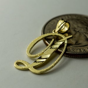 May include: A gold-colored initial 'D' pendant charm, with a diamond-cut design, next to a US quarter dollar coin.