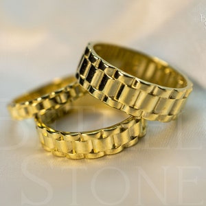 May include: Three gold-tone rings with a watch band design. The rings are stacked on top of each other.
