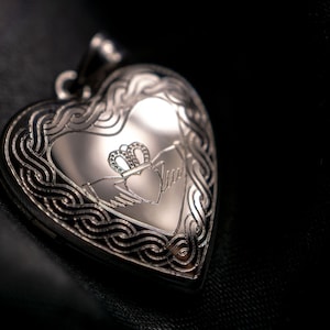 Puede incluir: Un medallón de plata en forma de corazón con un diseño de nudo celta y un símbolo Claddagh grabado en la parte delantera.