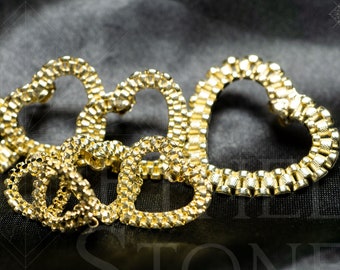 May include: A gold heart-shaped chain necklace with multiple links. The chain is made of small, interlocking pieces that form a heart shape. The necklace is lying on a black fabric background.